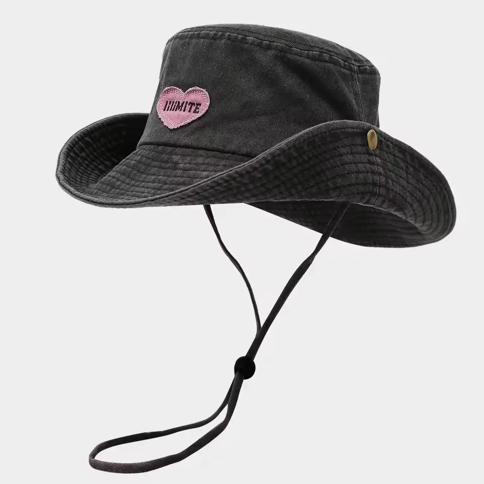 Black bucket hat with pink heart and text on a light gray background