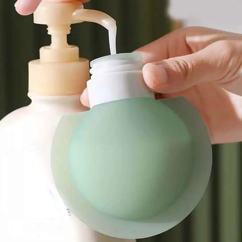 A close-up of a hand holding a translucent mint green silicone bottle cap or bottle cover over a white pump bottle, with liquid being dispensed.