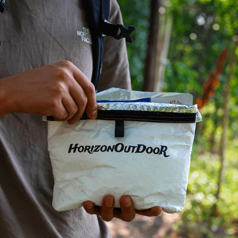 Person holding a white bag with 'Horizon Outdoor' branding outdoors.