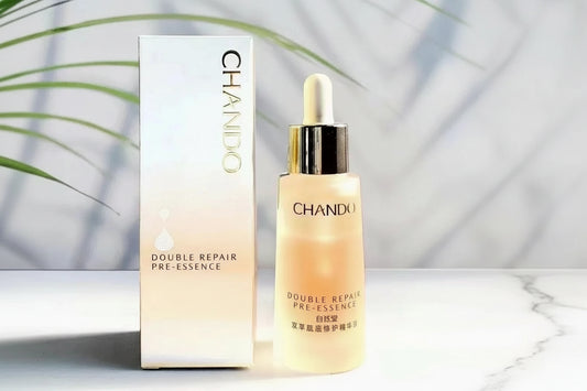 CHANDO Double Repair Pre-Essence skincare serum shown with its white and pale pink box and a frosted dropper bottle, photographed on a light surface with soft leaf shadows.