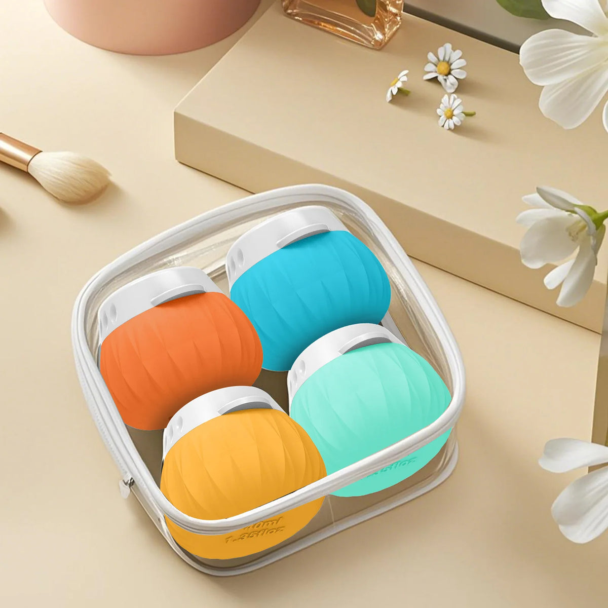 Four silicone personal care or beauty devices in orange, blue, yellow, and mint green, arranged inside a clear zippered square case on a beige surface with decorative props.