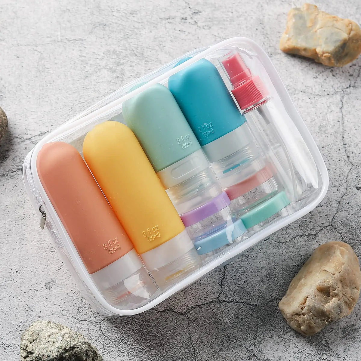 Set of colorful travel bottles in a clear case on a textured surface with rocks.