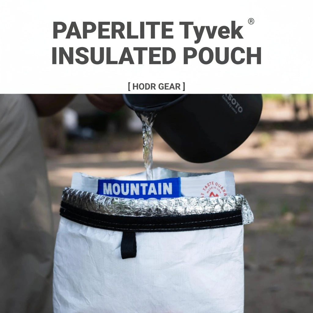 A white insulated pouch with black branding and a silver foil-lined opening, shown outdoors with a person pouring hot water from a black mug into it. Large text at the top reads 'PAPERLITE Tyvek INSULATED POUCH' .