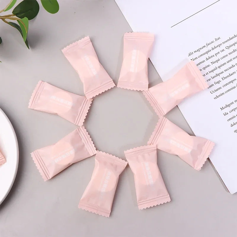 Pink packets arranged in a circular pattern on a light gray surface with a white paper and green leaves in the background.