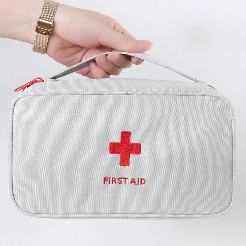 Hand holding a gray first aid kit with a red cross and 'FIRST AID' text on a white background