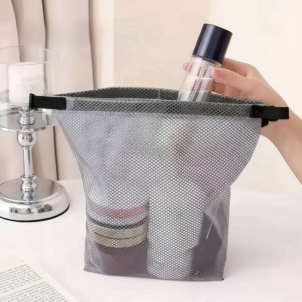 A gray mesh cosmetic storage bag with black handles is shown on a tabletop, holding skincare items. A hand is holding a bottle above the bag, and text overlays describe the large opening and capacity.