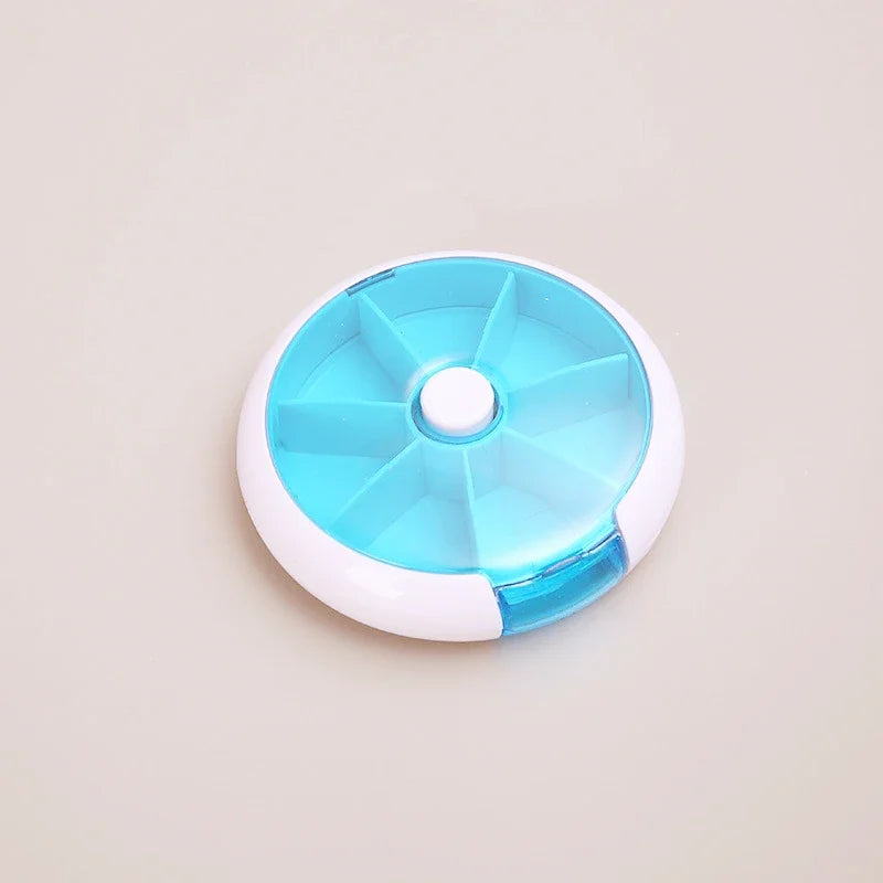 A round pill organizer container with a translucent light blue top and white base, photographed on a plain light beige background.