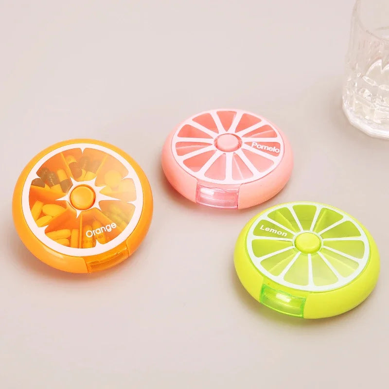 Three colorful pill organizers shaped like an orange, pink lemon, and green lemon on a light surface.