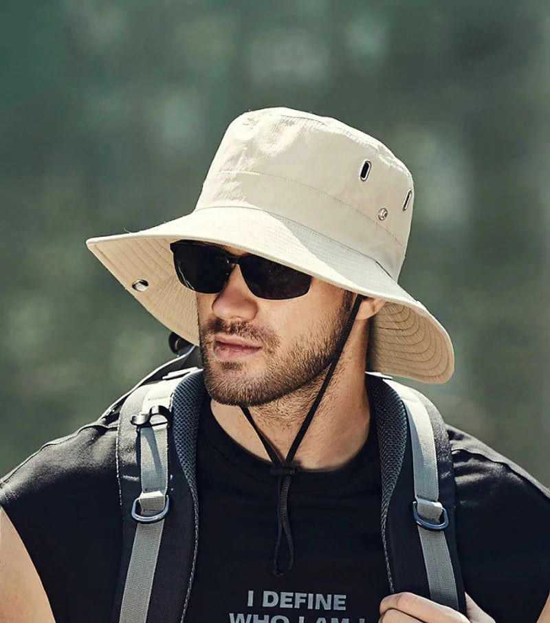 Man wearing a beige bucket hat and sunglasses with a blurred natural background