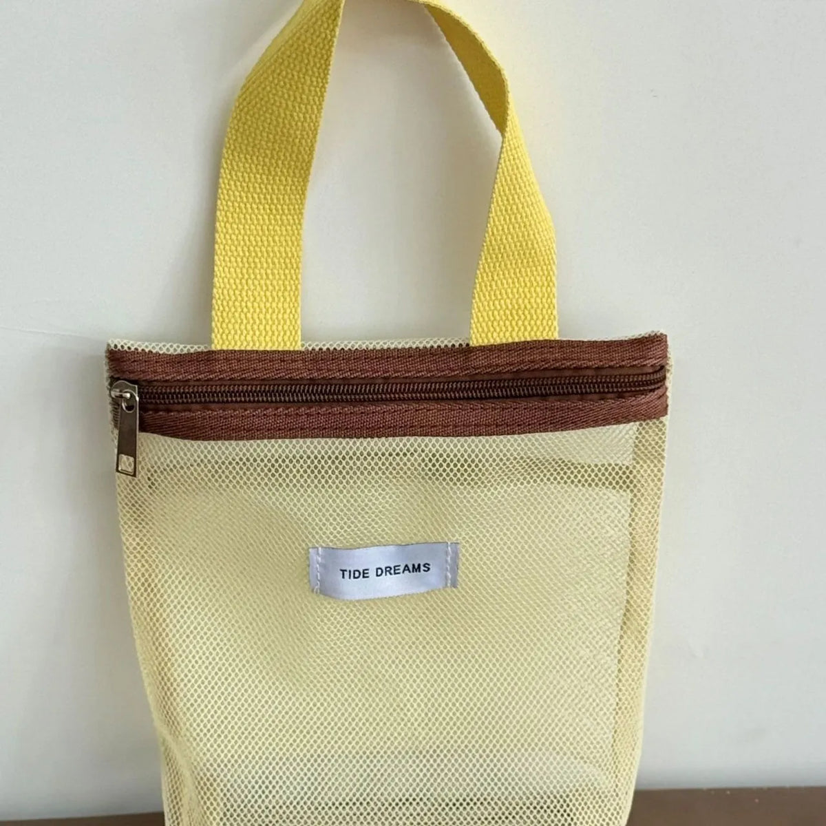 Mesh tote bag with yellow handles and brown zipper on a white background