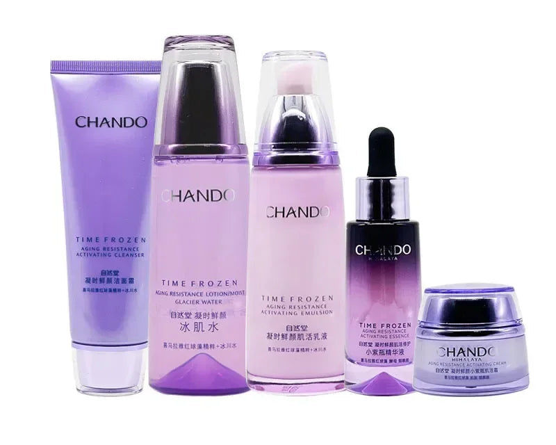 A five-piece CHANDO Time Frozen skincare set arranged on a white background, featuring a lavender tube, a tall purple bottle, a pink pump bottle, a black dropper bottle, and a small purple jar.