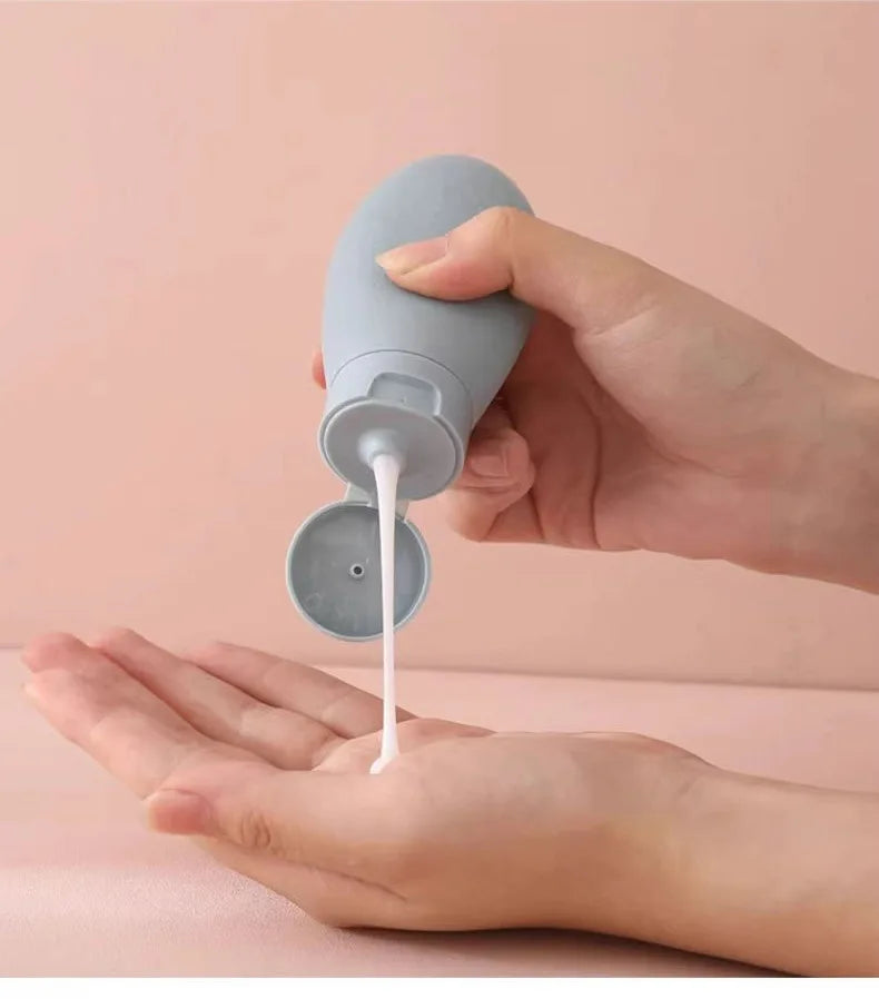 Hand holding a gray silicone bottle dispensing white liquid onto another hand against a pink background