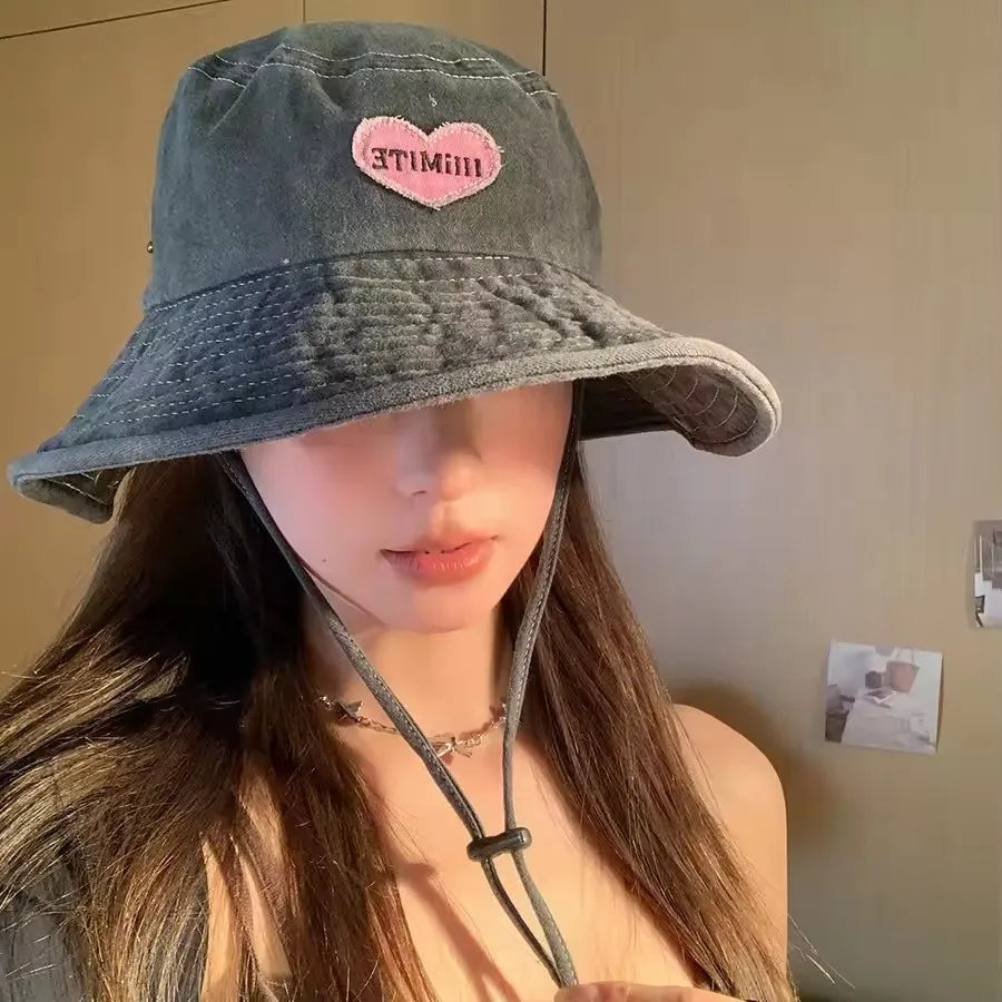 Person wearing a denim bucket hat with a pink heart design on a plain background