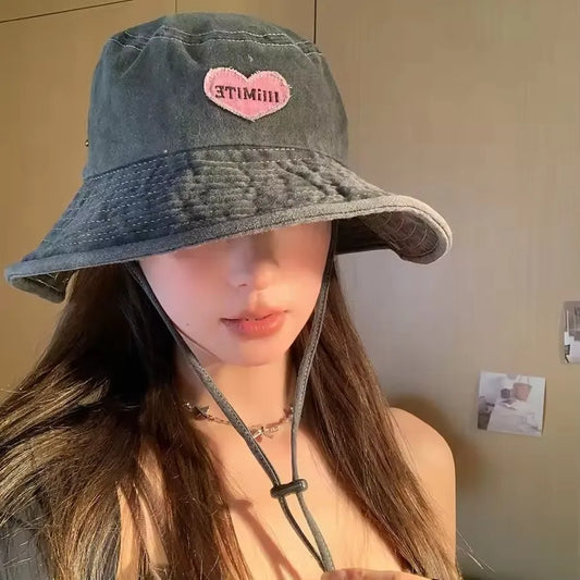 Person wearing a denim bucket hat with a pink heart design on a plain background