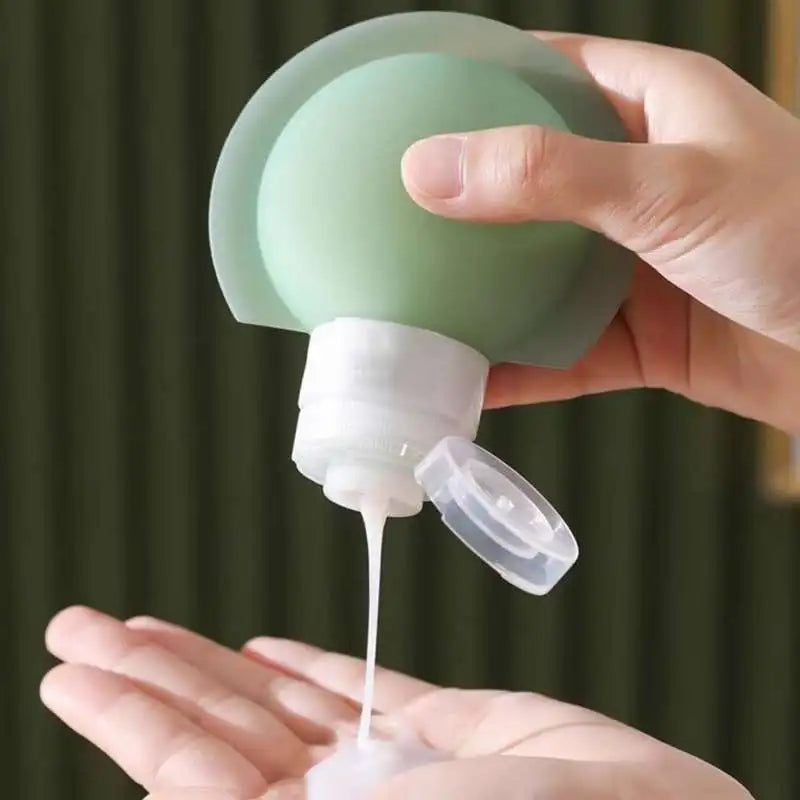 A hand holds a translucent mint green squeeze bottle dispensing a white cream or lotion into another hand, with a dark olive-green curtain in the background.