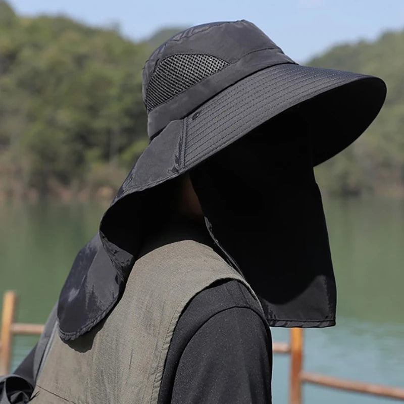 Person wearing a black wide-brimmed hat with neck flap outdoors by a body of water.