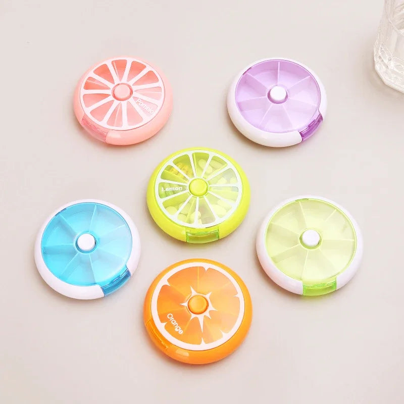 Six small round citrus-themed organizer cases in pink, purple, blue, green, yellow, and orange, arranged on a light beige surface.