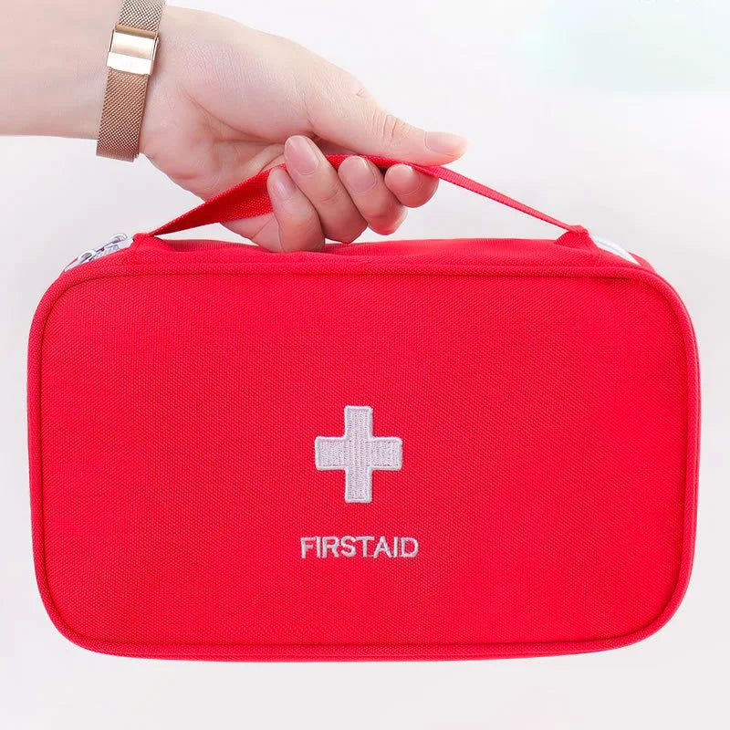 Red first aid kit with a white cross and 'FIRSTAID' text, held by a hand on a light gray background.